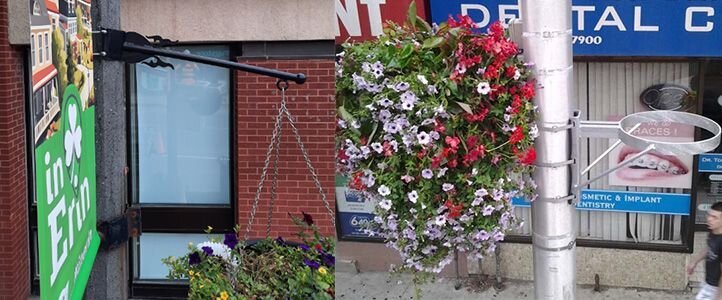 Old, bent hanging floral arm showing wear compared to a newer floral hoop holding a flower basket securely on a street pole.